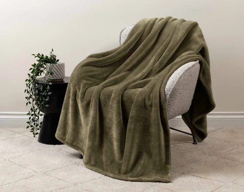 Our Velveteen Throw in Fir draped over a beige chair in a white living room.