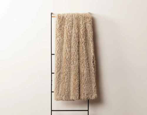 Front view of our Oat Soft Mink Throw draped over a tall rack against an empty white wall.