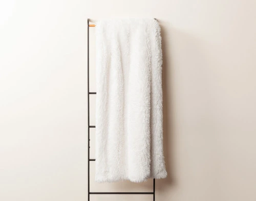 Front view of our White Soft Mink Throw draped over a tall rack against an empty white wall.