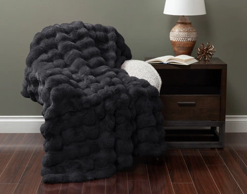 Front view of our Bubble Faux Fur Throw in Soot draped over a small armchair in a green fall living room.