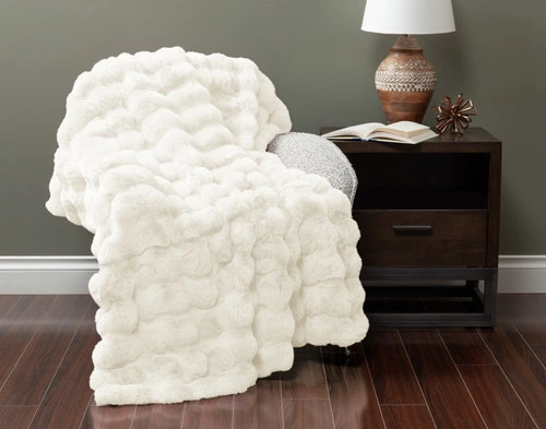 Front view of our Bubble Faux Fur Throw in White draped over a small armchair in a green fall living room.