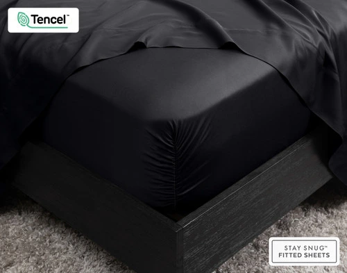 Close-up of the corner on our BeechBliss TENCEL™ Modal Fitted Sheet in Black snugly fit over a mattress with a flat sheet draped on top.