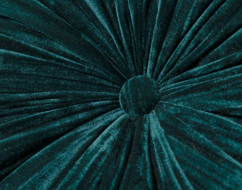 Angled view of our Ocean Pleated Velvet Round Cushion leaning against the arm of a small grey armchair.