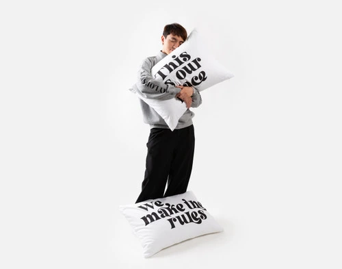 Front view of a man standing and hugging a pillow in one of our Our Place & Our Rules pillowcases.