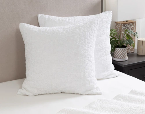 Angled view of our Crinkle Euro Shams in White leaning against a headboard on a bed dressed in white sheets.