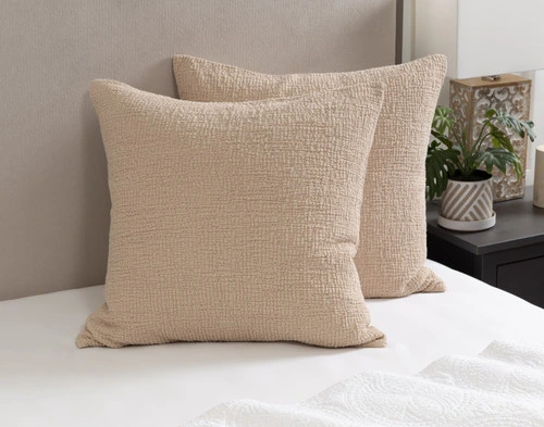 Angled view of our Crinkle Euro Shams in Sand leaning against a headboard on a bed dressed in white sheets.