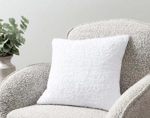 Notre housse de coussin Crinkle Square en blanc posée sur un fauteuil dans une pièce simple.