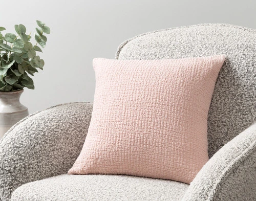 Our Crinkle Square Cushion Cover in Peony sitting on an armchair in a simple room.