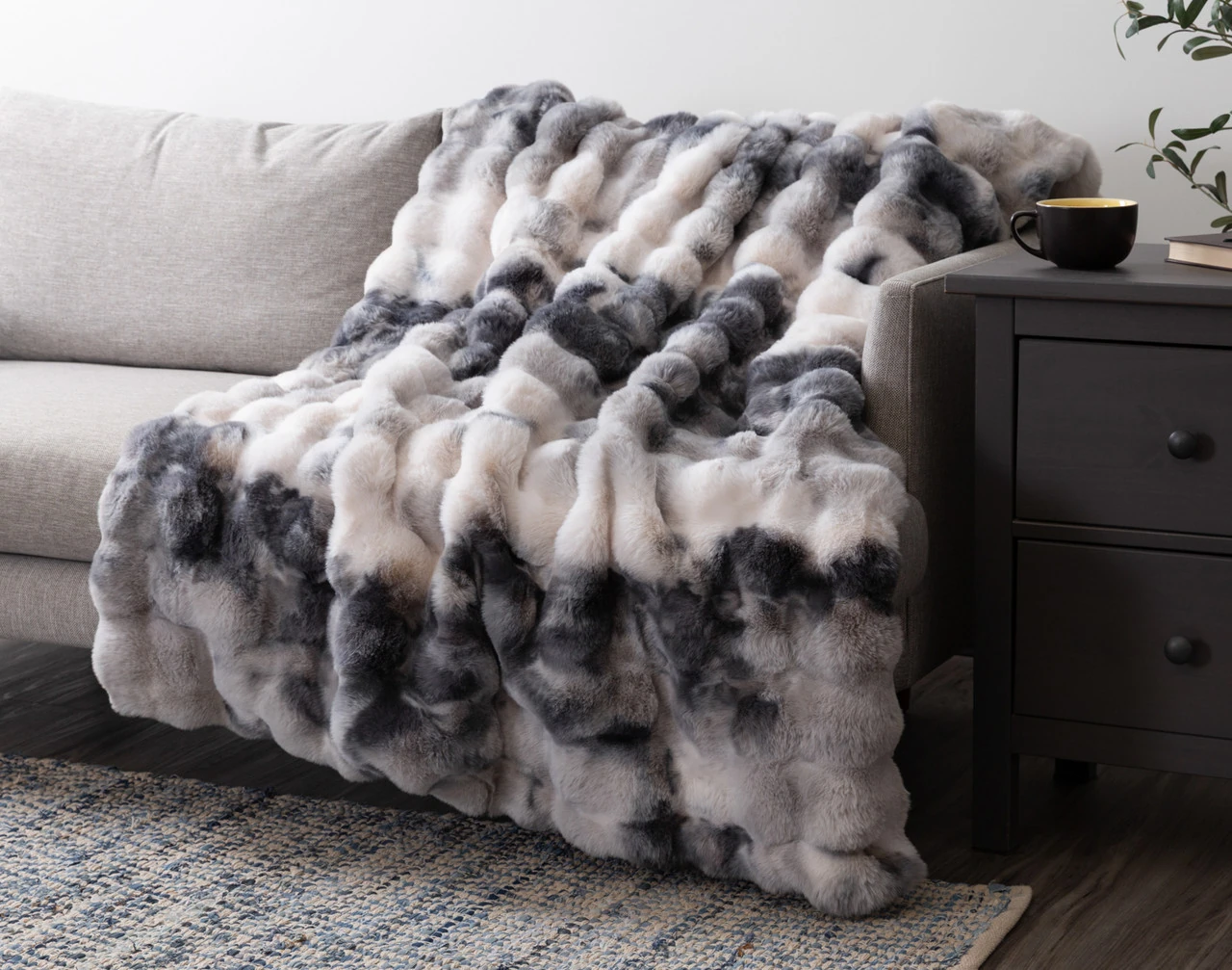 Our Bubble Faux Fur Throw in Deep Pond draped over a grey couch.