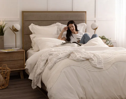 Angled view of a woman relaxing in a bed dressed in our Savary collection.