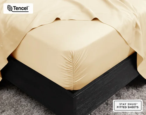 Close-up of the corner on our BeechBliss TENCEL™ Modal Fitted Sheet in Cornsilk snugly fit over a mattress with a flat sheet draped on top.