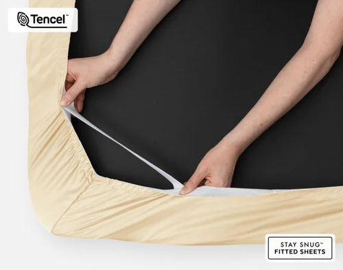 Bottom side of our BeechBliss TENCEL™ Modal Fitted Sheet in Cornsilk with two hands showing the Snug Fit elastics holding it tightly on the mattress.