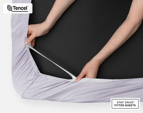 Bottom side of our BeechBliss TENCEL™ Modal Fitted Sheet in Lavender with two hands showing the Snug Fit elastics holding it tightly on the mattress.