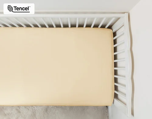 Top view of our Cornsilk BeechBliss TENCEL™ Modal Crib-Sized Fitted  Sheet dressed over a small white crib mattress.