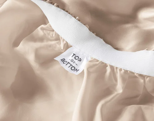 Close-up of a tag reading "Top / Bottom" on the inside edge of our Champagne Silk Blend Fitted Sheet.