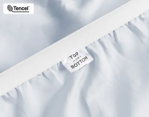 Close-up on the stretched elastic edge and tag stating "Top / Bottom" on our Eucalyptus Luxe TENCEL™ Lyocell Fitted Sheet in Blue Chalk.