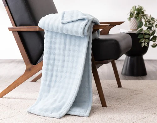 Angled view of our Powder Blue Bubble Breeze Throw draped over a chair touching the floor.