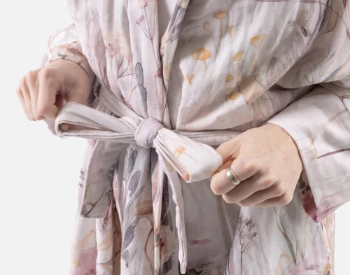 Close-up of two hands tying the belt on our Bamboo Cotton Gauze Bathrobe in Peach Blossom.