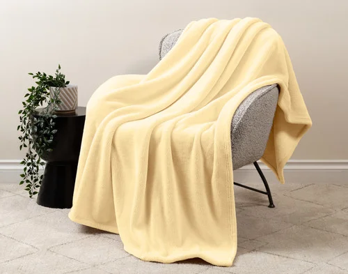 Our Velvet Plush Throw in Lemon Ice draped over a beige chair in a white living room.