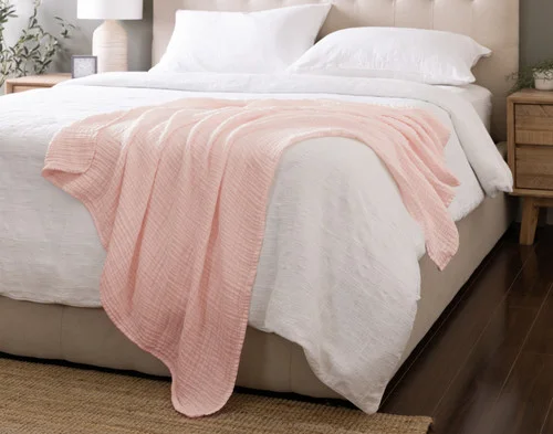 Our Bamboo Gauze Throw in Blossom draped over the corner of a bed.