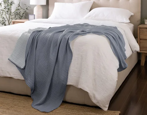 Our Bamboo Gauze Throw in Seaside draped over the corner of a bed.