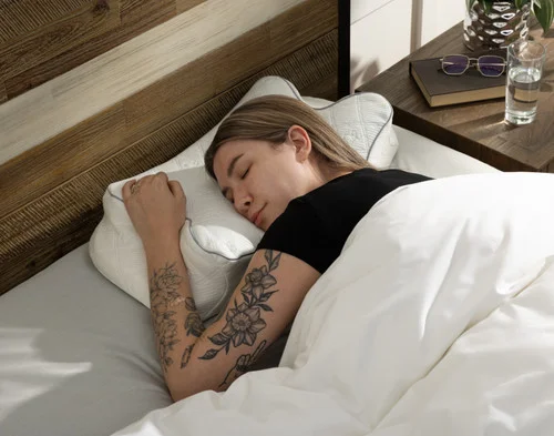 Woman resting comfortably on her stomach in bed on a Butterfly Memory Foam Pillow.