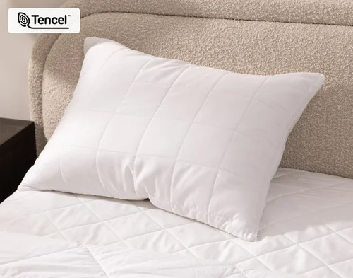 Angled view of a pillow in our Ambience TENCEL™ Pillow Protector resting against a headboard.