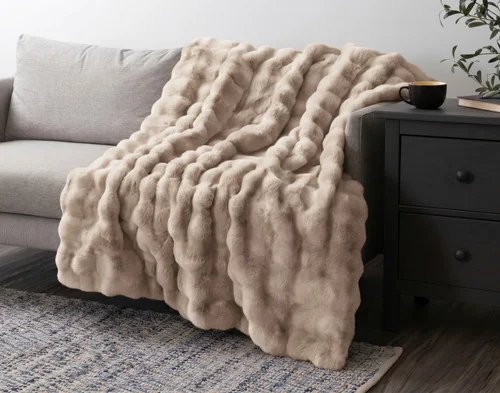 Our Bubble Faux Fur Throw in Champagne draped over a grey couch.