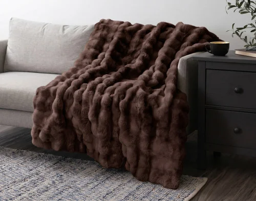 Our Bubble Faux Fur Throw in Truffle draped over a grey couch.