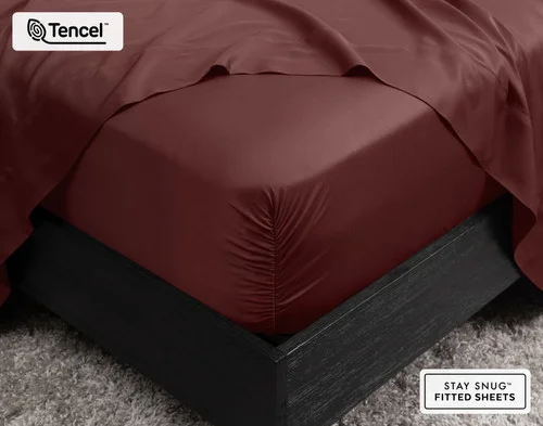 Close-up of the corner on our BeechBliss TENCEL™ Modal Fitted Sheet in Mahogany snugly fit over a mattress with a flat sheet draped on top.