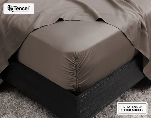 Close-up of the corner on our BeechBliss TENCEL™ Modal Fitted Sheet in Bark snugly fit over a mattress with a flat sheet draped on top.