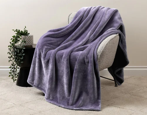 Our Velvet Plush Throw in Violet Smoke draped over a beige chair in a white living room.