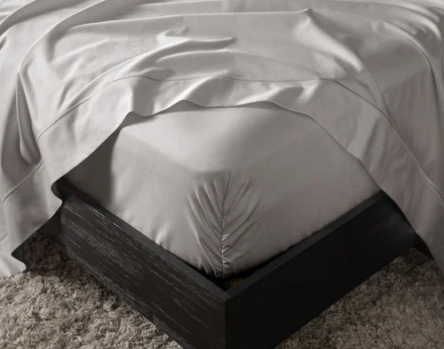 Close-up on the fitted sheet of our Grey Mist Luxor Egyptian Cotton Sheet Set over a mattress, with a matching flat sheet draped overtop.
