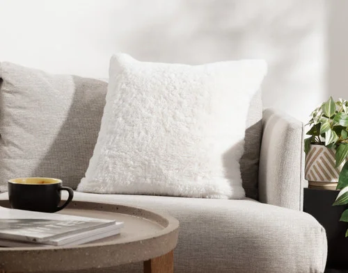 Angled view of our Ivory Poodle Faux Fur Square Cushion resting on a couch.