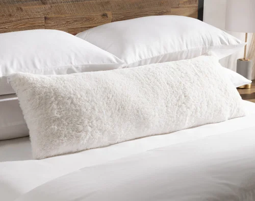 Angled view of our Ivory Poodle Faux Fur Lumbar Pillow resting on a bed.