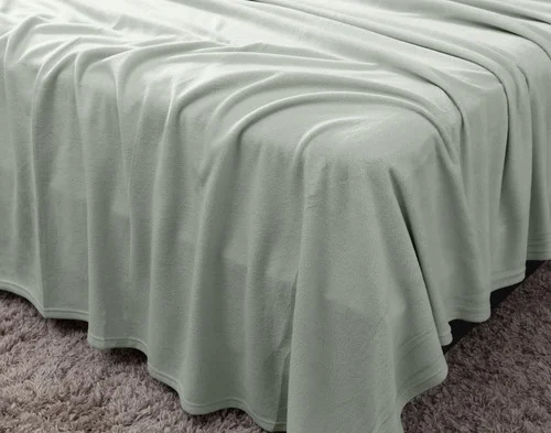 Angled view of a draped flat sheet over the corner of a bed fitted with our Cuddle Fleece Sheet Set in Fern.