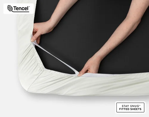 Close-up on two hands stretching the elastic snug fit band on the corner of our Eucalyptus Luxe Fitted Sheet in Oyster.