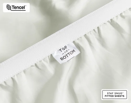 Close-up on the stretched elastic edge and tag stating "Top / Bottom" on our Eucalyptus Luxe Fitted Sheet in Oyster.