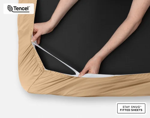 Close-up on two hands stretching the elastic snug fit band on the corner of our Eucalyptus Luxe Fitted Sheet in Sandalwood.