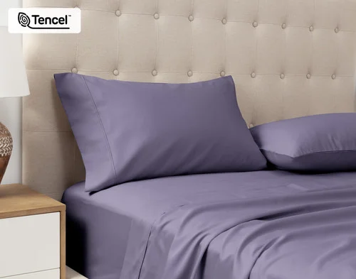 Angled view of our Eucalyptus Luxe Pillowcases in Purple Basil sitting against a headboard of a beige queen bed.