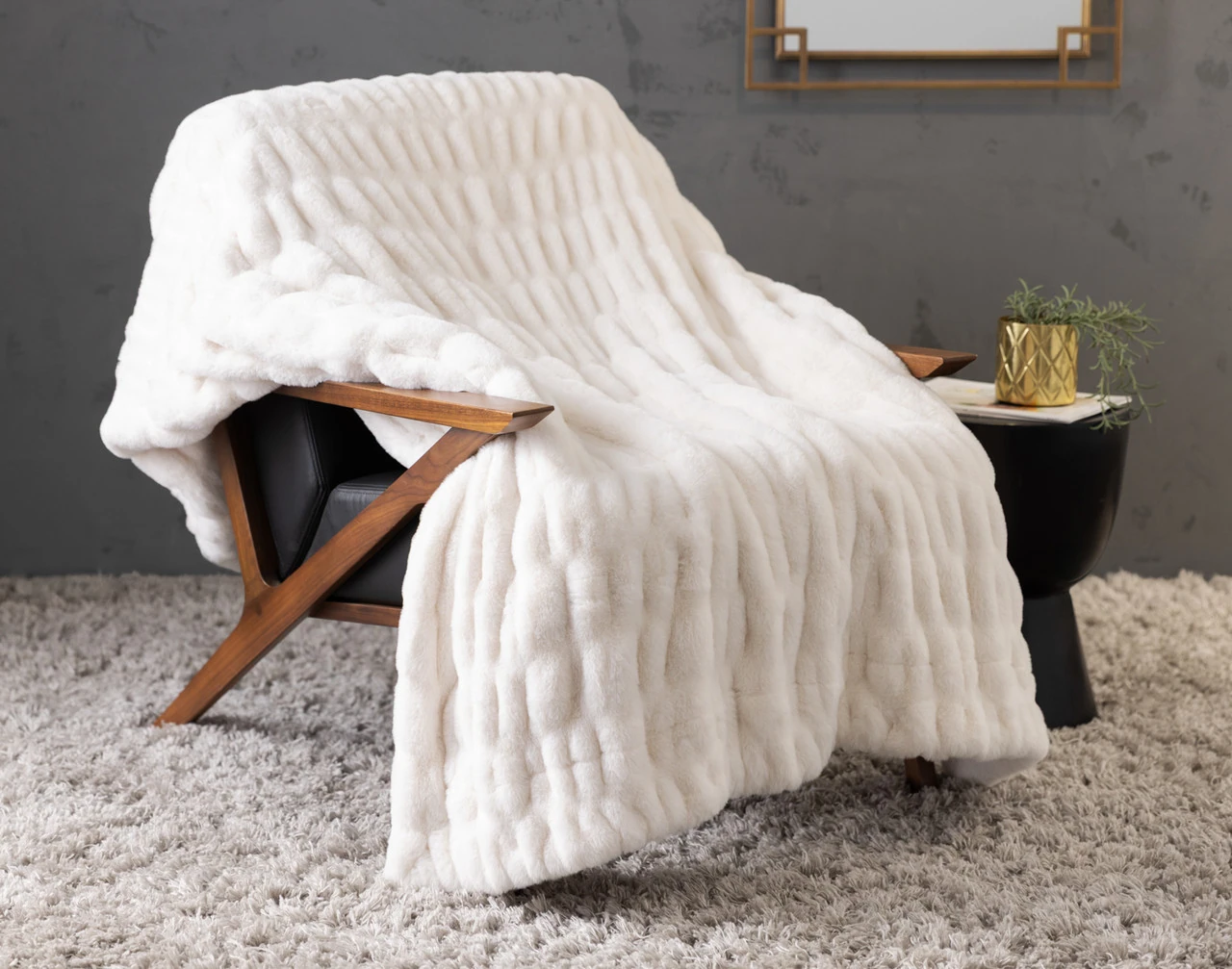 Our Cocoon Plush Throw in Cream draped over a chair in a grey room.
