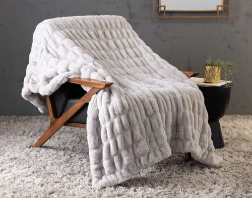 Our Cocoon Plush Throw in Silver draped over a chair in a grey room.