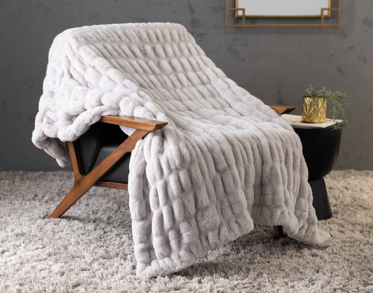 Our Cocoon Plush Throw in Silver draped over a chair in a grey room.