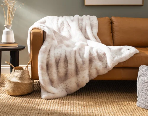 Our Animal Faux Fur Throw - Snow Leopard draped over a brown couch.