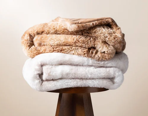Both of our Animal Faux Fur Throws sitting neatly on a stool.