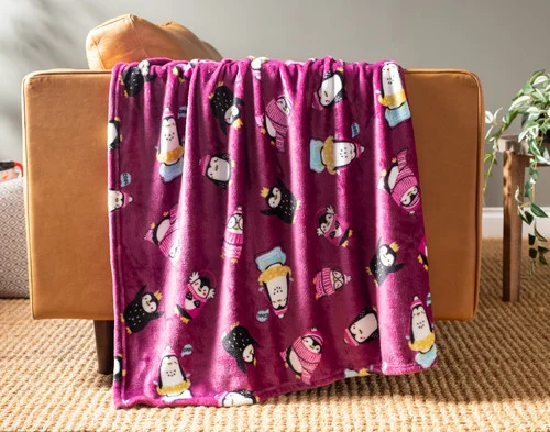 Our Holiday Fleece Throw - Winter Waddle draped over a brown couch.