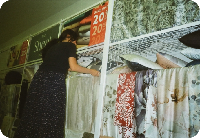 A QE Home graphic designer adjusts a print sign in the office's mock shop, with fabric product samples displayed on racks below.