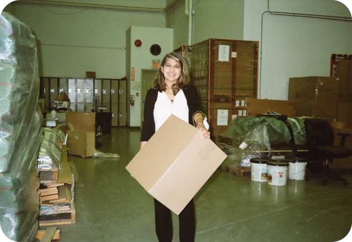 The office manager stands in the QE Home warehouse, holding a box of bedding products, ready for shipment.