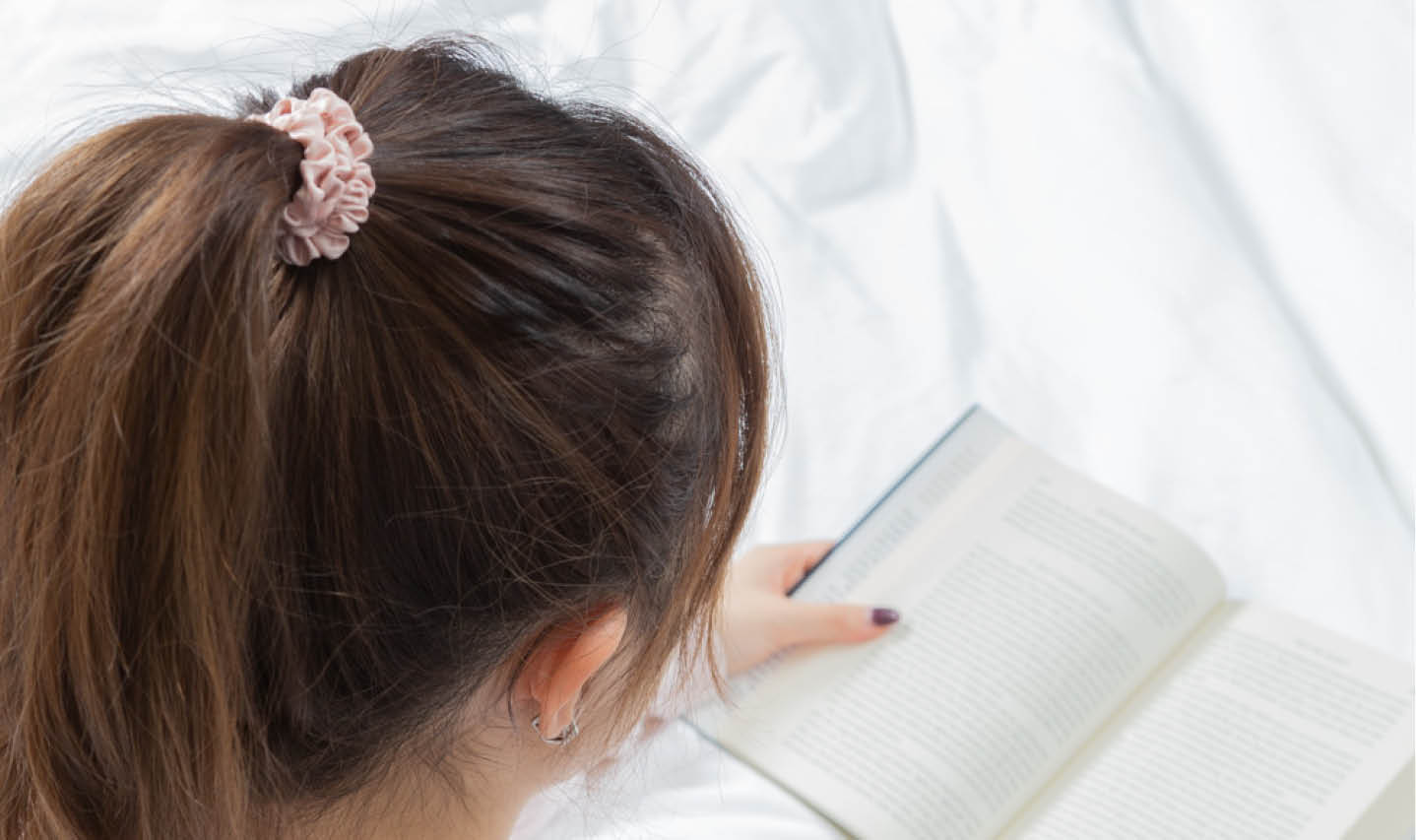 Top view of a woman reading with her ponytail in focus, being held in a blush pink mulberry silk scrunchie. Top view of a woman reading with her ponytail in focus, being held in a blush pink mulberry silk scrunchie.