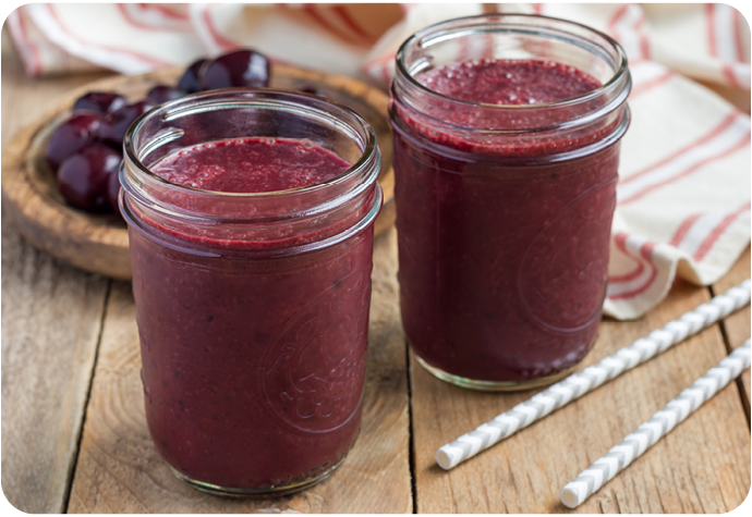 Angled view of two cherry smoothies sitting on a wooden table in glass cups.